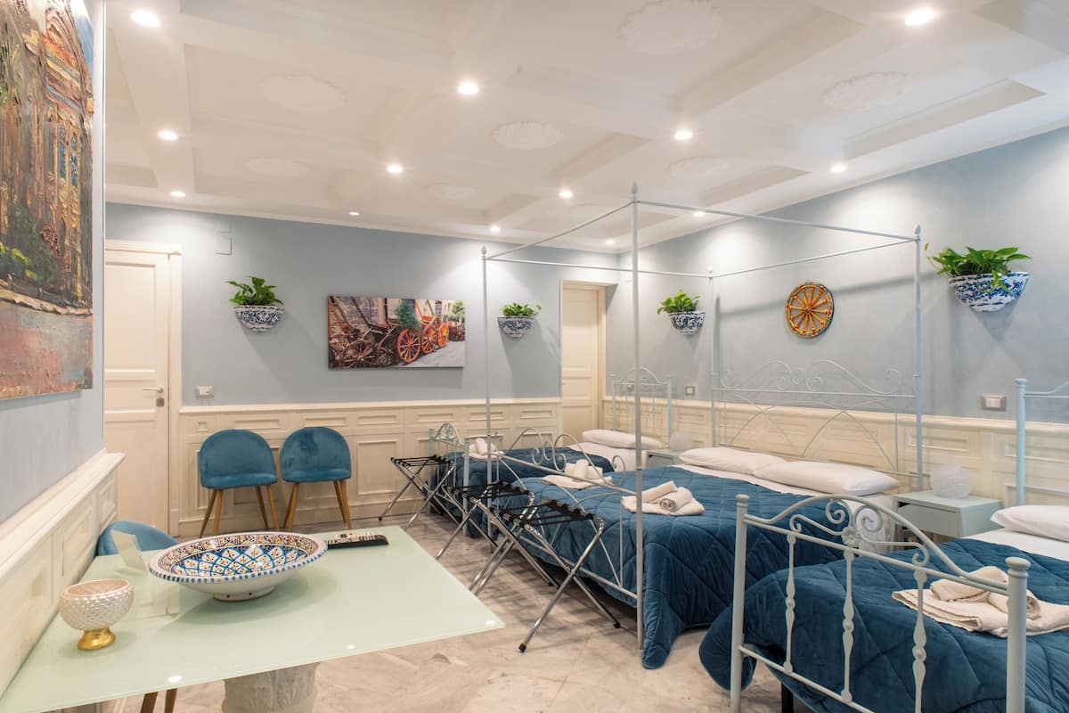 A bedroom with two beds, a dining table, chairs, a small table with a bowl, and potted plants.