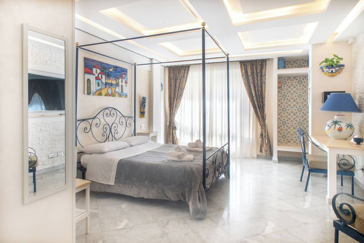 A bedroom with a four-poster bed, a desk with a lamp, and a chair.