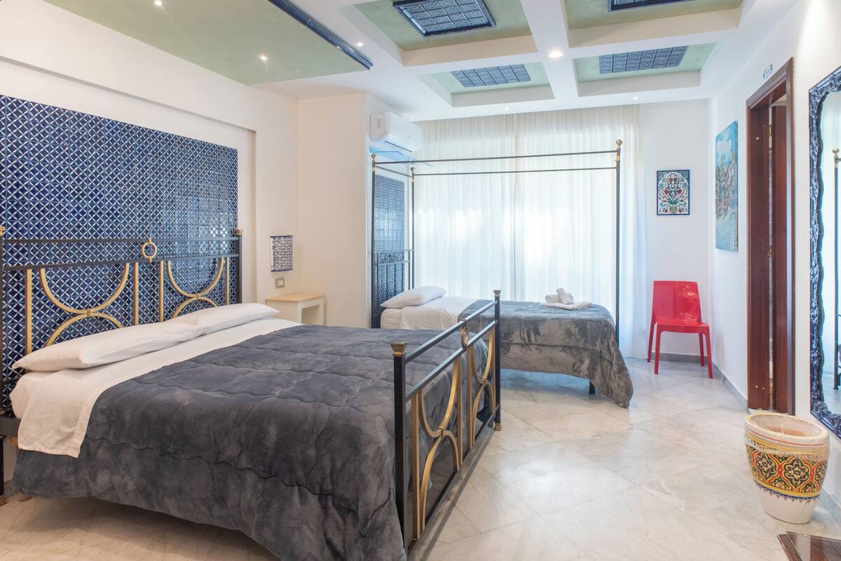 A hotel room with two beds, a red chair, a decorative wall, and a large mirror.