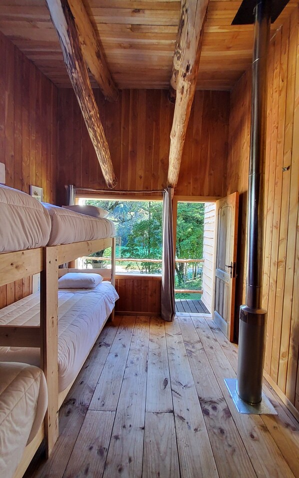 A wooden cabin with bunk beds, a chimney, and a view of greenery.