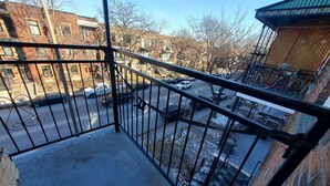 Ein Balkon mit Metallgeländer, der auf eine Straße mit parkenden Autos und Fahrrädern blickt.