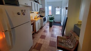 Eine kompakte Küche mit Kühlschrank, Herd und Schränken. Ein kleines Fenster und eine Tür mit Fußmatte sind vorhanden.