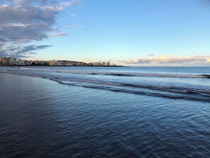 Une plage avec des vagues, une vue sur les gratte-ciel d’une ville en arrière-plan et un ciel dégagé.