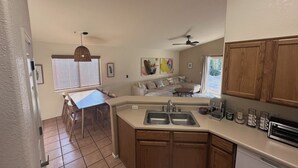 A modern kitchen with wooden cabinets, a built-in sink, and a dining area with a table and chairs. - Stylish Tucson Getaway • Pool • Hot Tub • Game Zone - Sleeps 7 (Oro Valley)