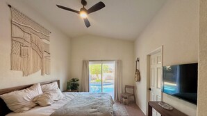 A bedroom with a bed, a ceiling fan, a TV, and a view of a swimming pool. - Stylish Tucson Getaway • Pool • Hot Tub • Game Zone - Sleeps 7 (Oro Valley)