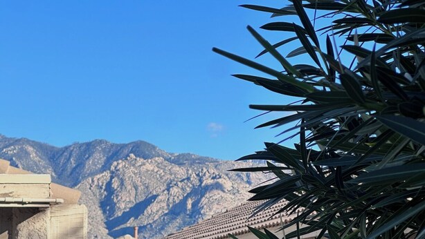 A residential area with a mountain backdrop, featuring a house with a tiled roof, a brick wall, and a gate. - Stylish Tucson Getaway • Pool • Hot Tub • Game Zone - Sleeps 7 (Oro Valley)