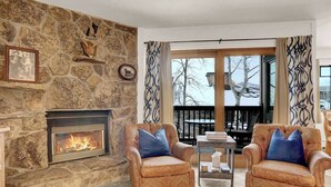 Ein gemütliches Wohnzimmer mit Kamin aus Stein, zwei Ledersesseln und Blick ins Freie.