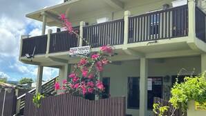 Un bâtiment à deux étages doté d’un balcon, d’une enseigne indiquant « Touch Therapies » et d’une clôture en bois ornée de plantes à fleurs.