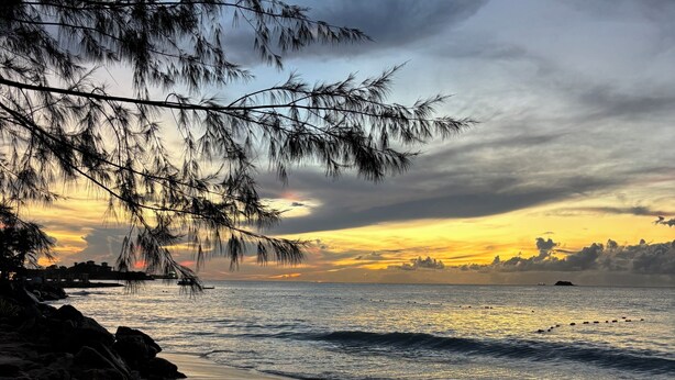 Une plage parsemée d’empreintes, un rivage rocheux et un coucher de soleil sur l’océan.