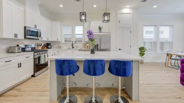 Una cocina moderna con armarios blancos, una isla central con taburetes de bar e iluminación colgante.