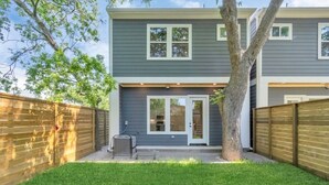 Una casa de dos pisos con fachada gris, una puerta principal y un pequeño patio con una parrilla.