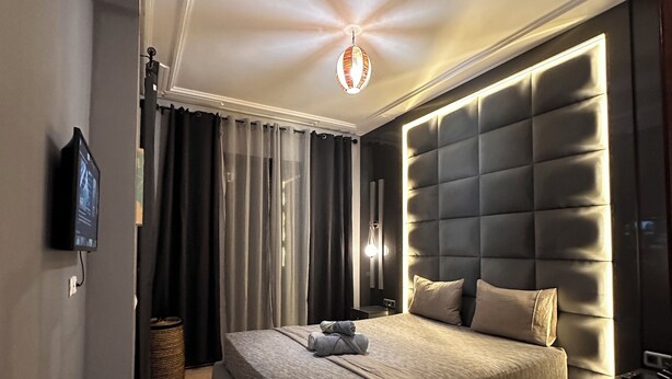 A modern bedroom with a large bed, a tufted headboard, and a ceiling light fixture. - Marrakech Oasis 2-bedroom apartment with direct garden and pool access with AC (Marrakech)