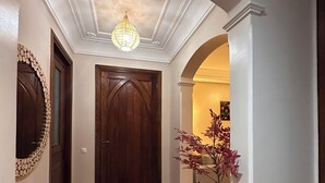 A hallway with a wooden door, a chandelier, a patterned rug, and a plant. - Marrakech Oasis 2-bedroom apartment with direct garden and pool access with AC (Marrakech)