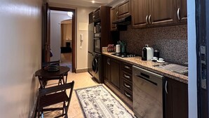 A compact kitchen with dark wooden cabinets, a built-in oven, a microwave, and a gas stove. There is a small dining area with a table and chairs. - Marrakech Oasis 2-bedroom apartment with direct garden and pool access with AC (Marrakech)