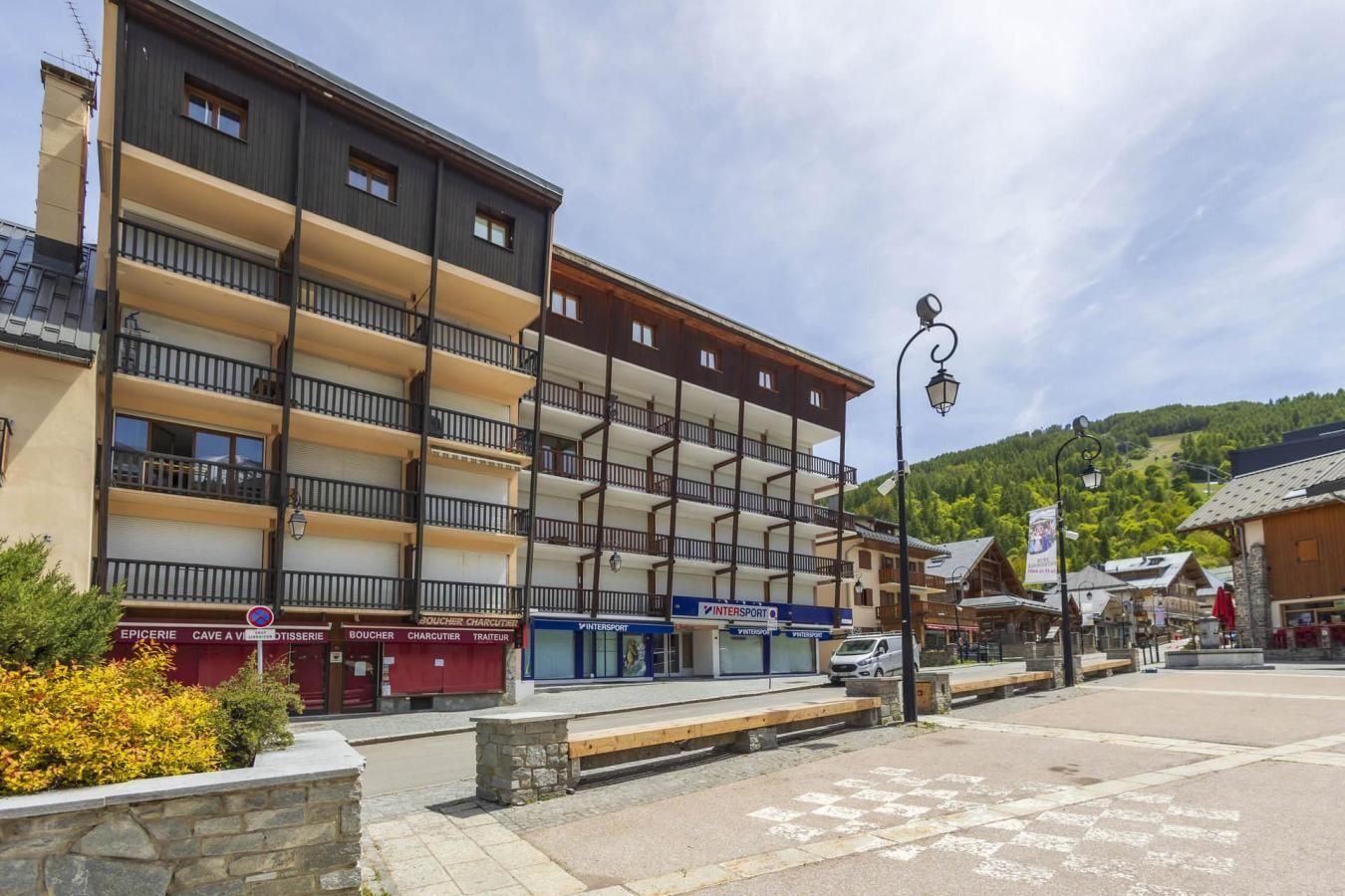 Um edifício de vários andares com varandas, um café e uma placa com a inscrição 'INTERSPORT'.