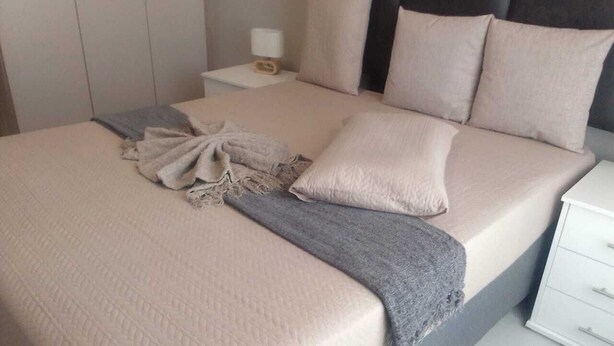 A neatly made bed with a grey throw blanket and pillows, a bedside table with a lamp, and a white nightstand. - Wonderful apartment in peaceful Midrand perfect for your stay (Midrand)