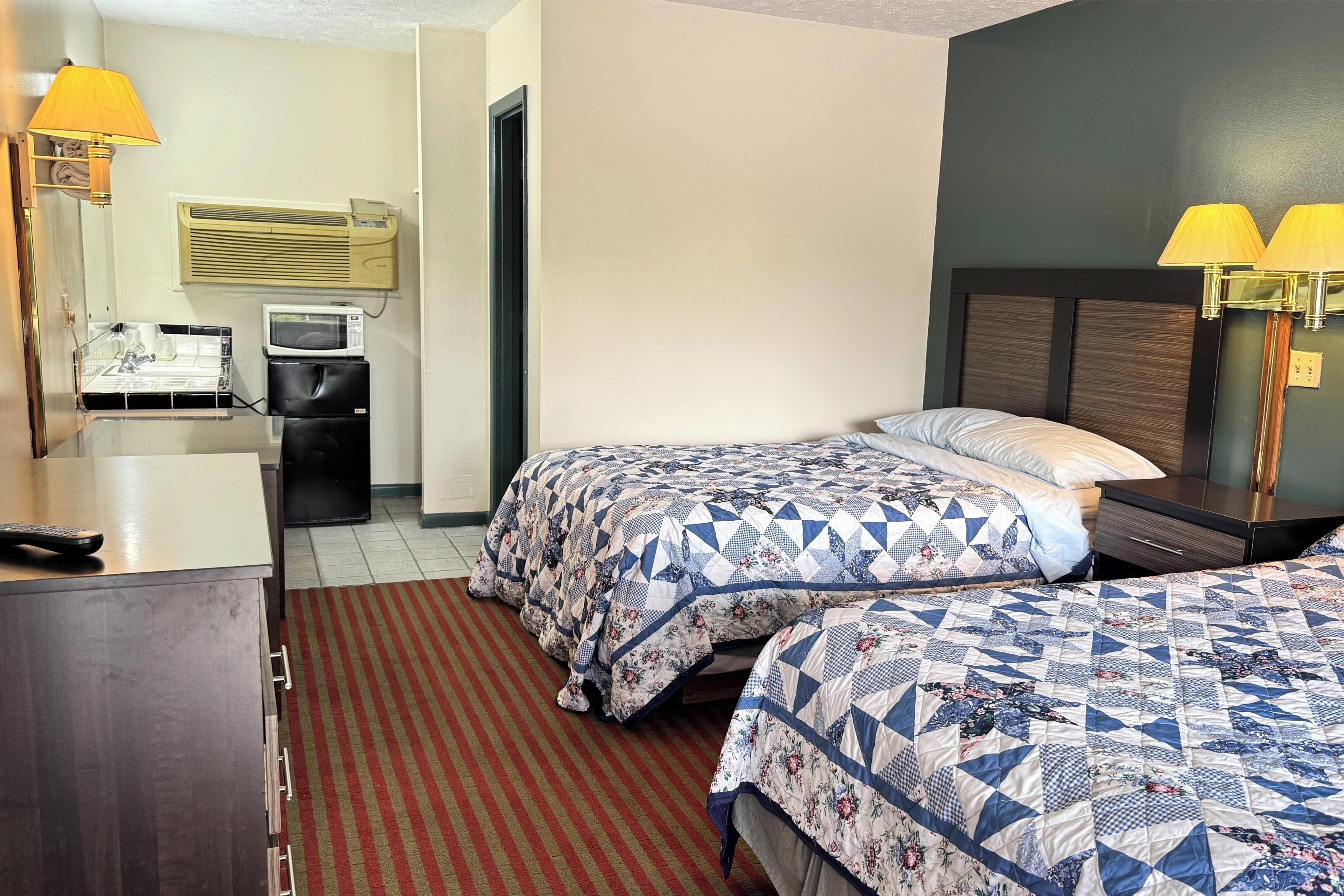 A hotel room with two beds, a desk, a refrigerator, a microwave, and a lamp.