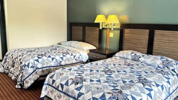 A hotel room with two beds, each with a floral-patterned quilt, a nightstand with a lamp, and a plain wall.