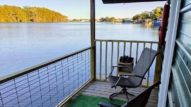 A balcony with a view of a lake, a chair, and a small table.