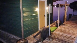 A wooden deck with a door leading to a building, a small outdoor seating area, and a view of the water.