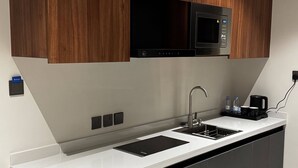 A modern kitchen with wooden cabinets, a black microwave, a sink, and a built-in refrigerator. - Royal Edition Hotel Apartments (Buraydah)