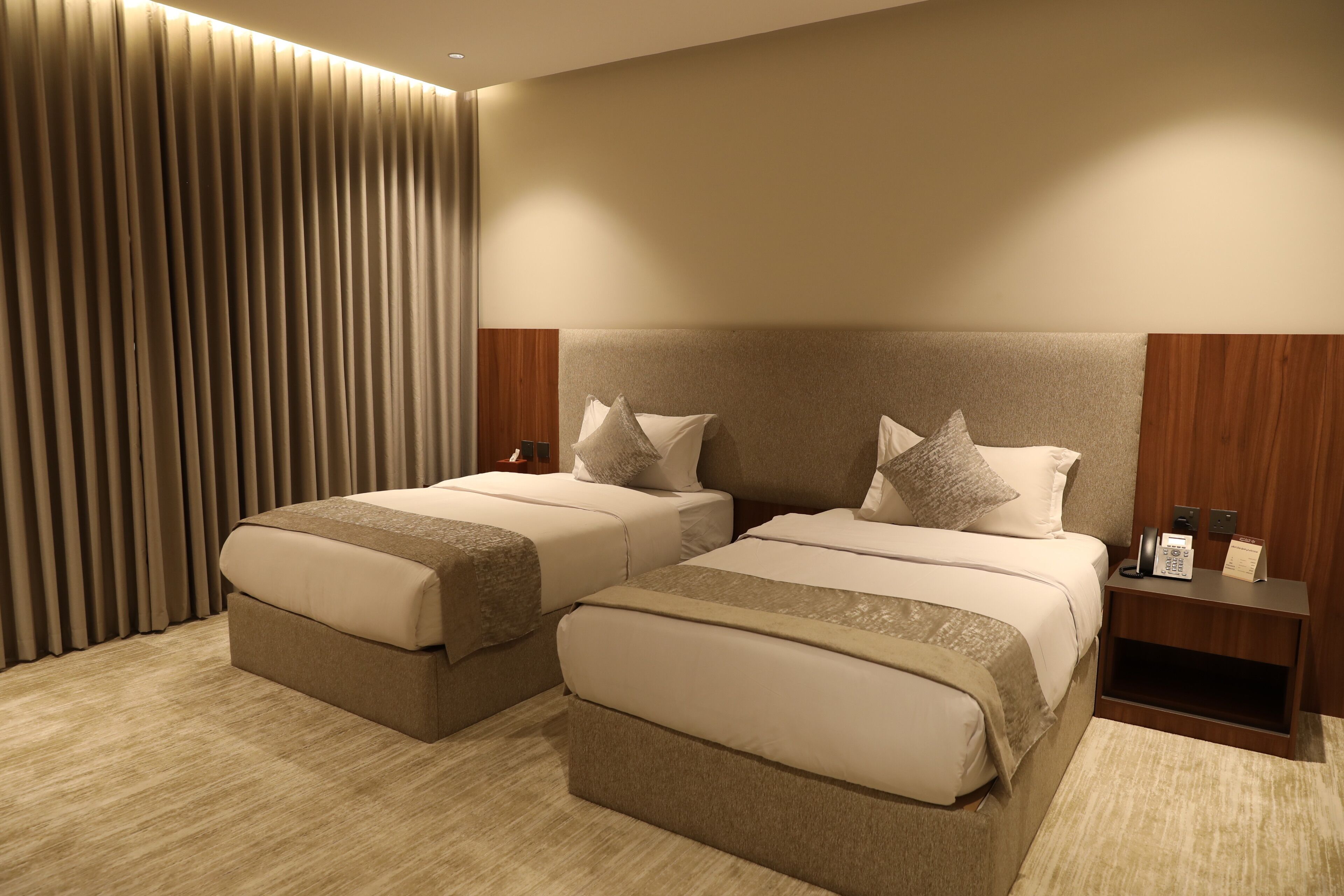 Una habitación de hotel con dos camas, un cabecero de madera, una mesita de noche con un teléfono y una cortina.