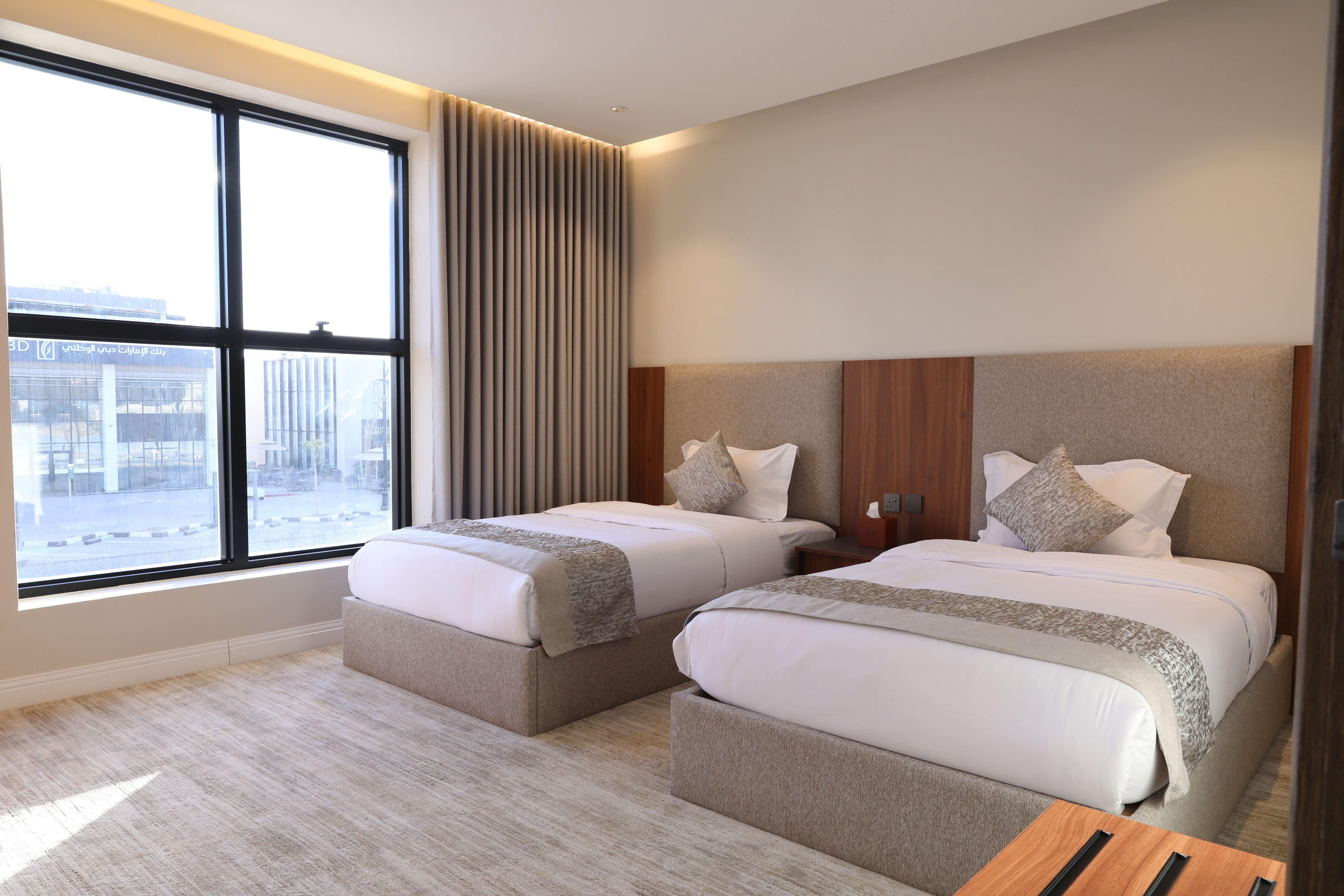 Habitación de hotel con dos camas, un ventanal grande y vistas a un edificio.