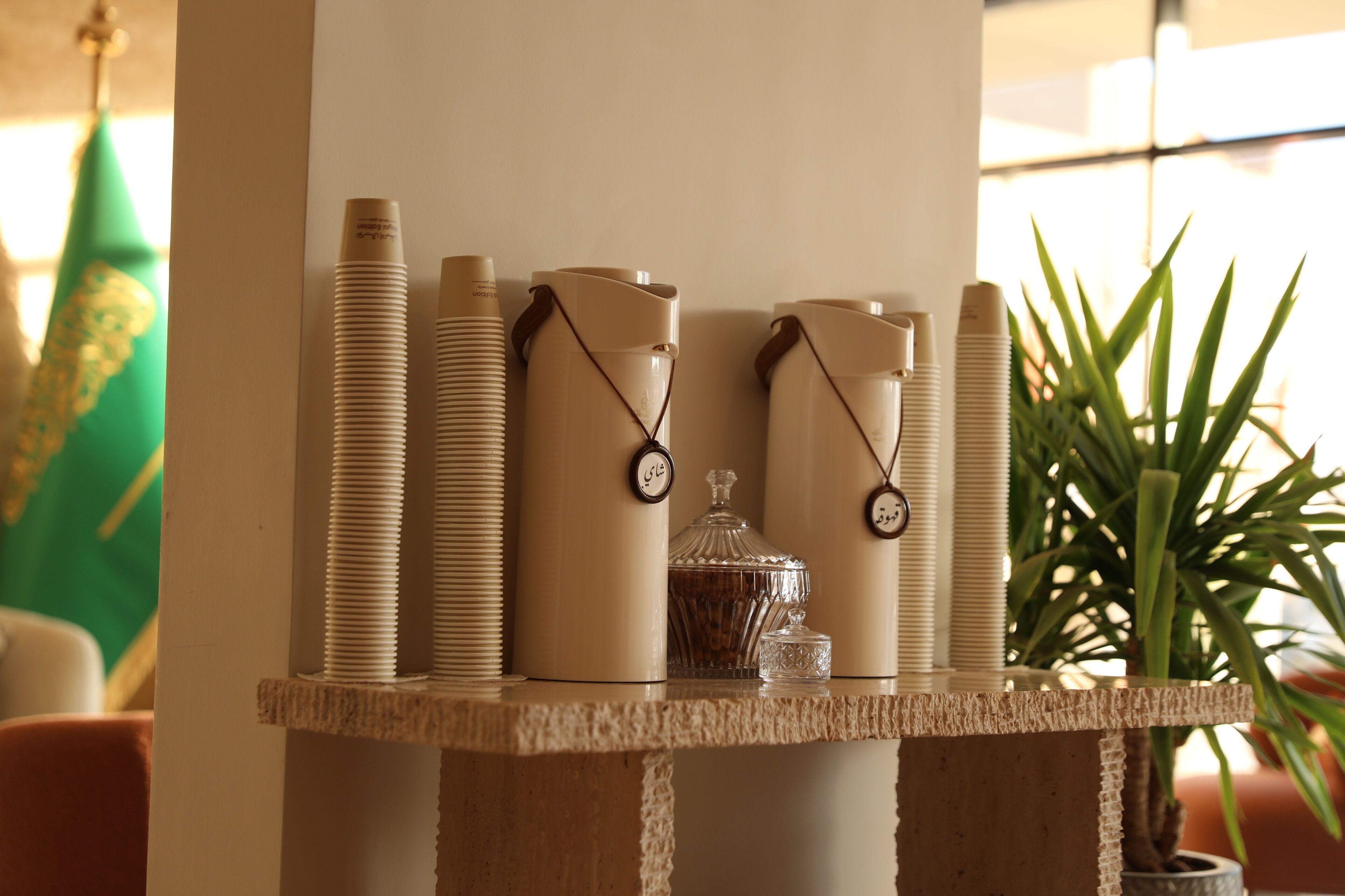 A table with stacked items, a glass container, and a potted plant.