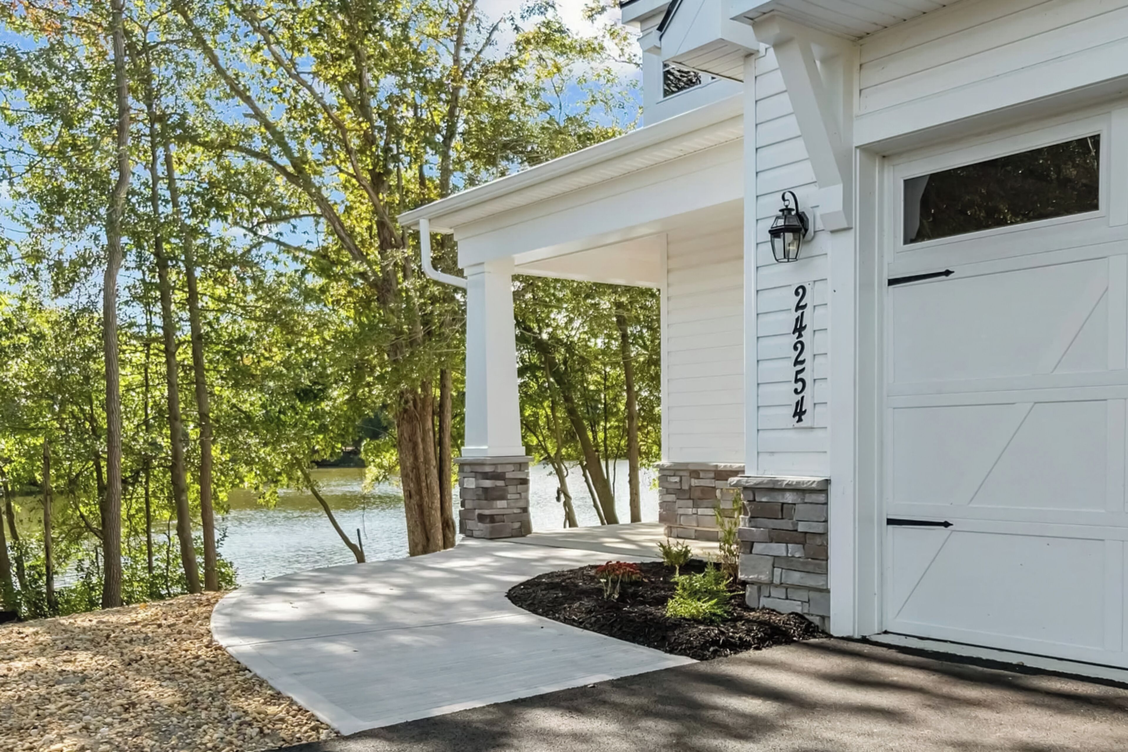 A house with a white garage, stone pillars, and a view of a lake.