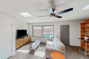 Ein modernes Wohnzimmer mit Fernseher, Holzschränken, einer Couch, einem Couchtisch und einem Deckenventilator.