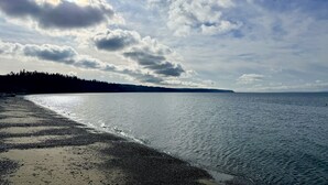 Une plage avec une mer calme, un ciel dégagé et une ligne d’arbres à l’horizon.