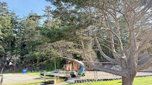 Une aire de jeux avec un toboggan et des structures d’escalade, entourée d’arbres et d’une pelouse.