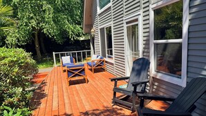 Une terrasse en bois, dotée de meubles d’extérieur, d’une rambarde et d’une maison avec de grandes fenêtres.