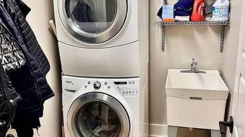 A laundry area with stacked washing machines, a shelf with cleaning supplies, and a small sink.