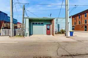 A small, single-story building with a red door and a garage door, surrounded by a wooden fence and utility poles. - 'Downtown Delight' w/ Patio! 1 Mi to Ball State (Muncie)
