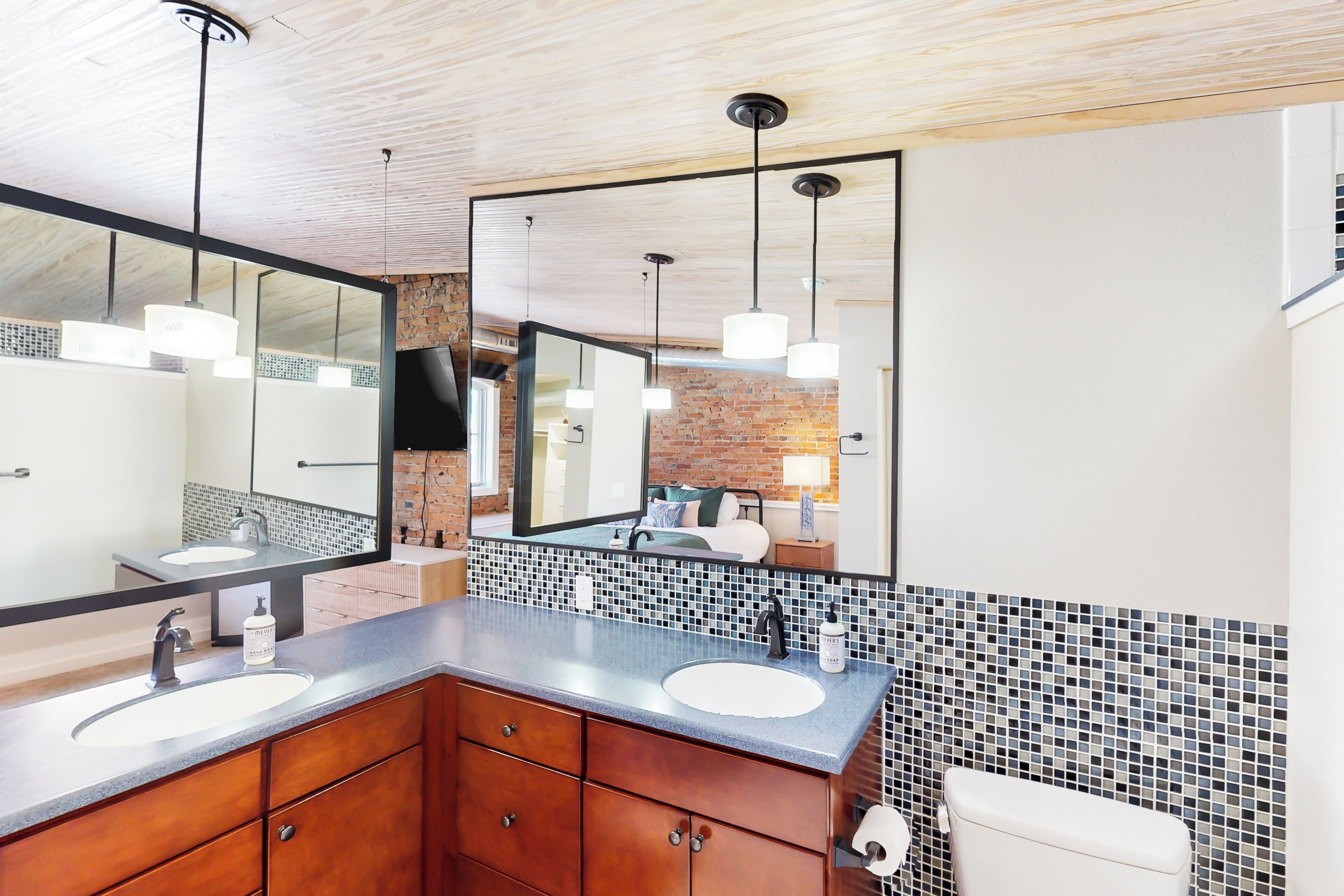 A modern bathroom with two sinks, wooden cabinets, a large mirror, and a tiled backsplash.