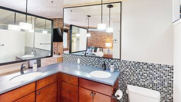 A modern bathroom with two sinks, wooden cabinets, a large mirror, and a tiled backsplash.