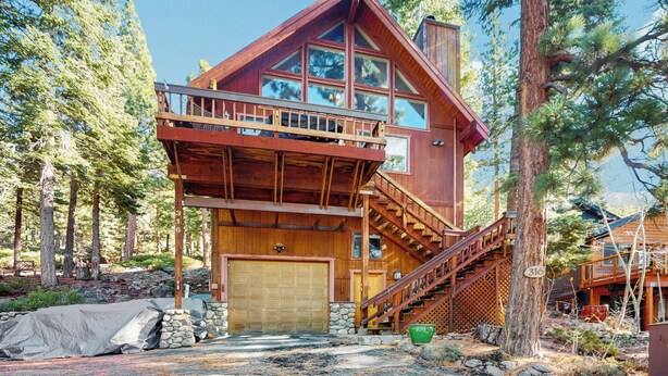 Une cabane en rondins à deux étages, dotée d’une terrasse en bois, d’un garage et d’un escalier menant à l’étage supérieur.