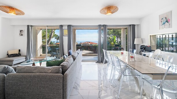 Una sala de estar moderna con una mesa de comedor de cristal, sofás grises y vistas al mar a través de amplios ventanales.