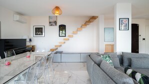 Una sala de estar moderna con una mesa de comedor de vidrio, sofá gris y una escalera con escalones de madera.
