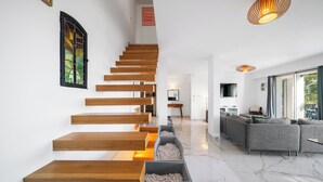 Un interior moderno con una escalera de madera, un sofá gris y un piso de mármol.