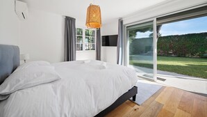 Un dormitorio moderno con una cama grande, televisión y vistas a un jardín a través de un ventanal corredero.