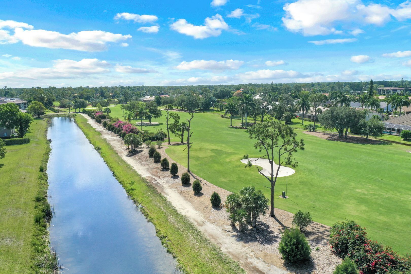 A golf course with a water channel, neatly trimmed grass, and a variety of trees.