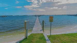 A wooden pier leading to a body of water with a warning sign, a grassy area, and a distant view of a bridge. - 🌴 Waterfront-Beach-Swimming-Fishing-Dock-Double sized private Balcony (Mary Esther)