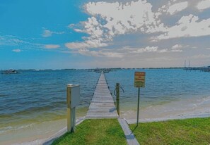 A wooden pier leading to a body of water with a warning sign, a grassy area, and a distant view of a bridge. - Waterfront-Beach-Swimming-Fishing-Dock-Double sized private Balcony (Mary Esther)