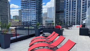 A rooftop terrace with red lounge chairs, a seating area, and a view of surrounding high-rise buildings. - Free Indoor Parking Old Montreal 4 (Montréal)
