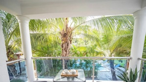 A balcony with two black wicker chairs, a glass table with a tray, and a view of palm trees and a pool. - Stylish 2BR in Sosua with Pool, Bbq, Fast Internet & Back up Generator (Sosúa)