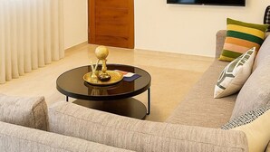 A living room with a sofa, a coffee table, a television, and a door. - Stylish 2BR in Sosua with Pool, Bbq, Fast Internet & Back up Generator (Sosúa)