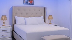 A bedroom with a large bed, bedside tables, a nightstand, a footstool, and a ceiling light. - Stylish 2BR in Sosua with Pool, Bbq, Fast Internet & Back up Generator (Sosúa)