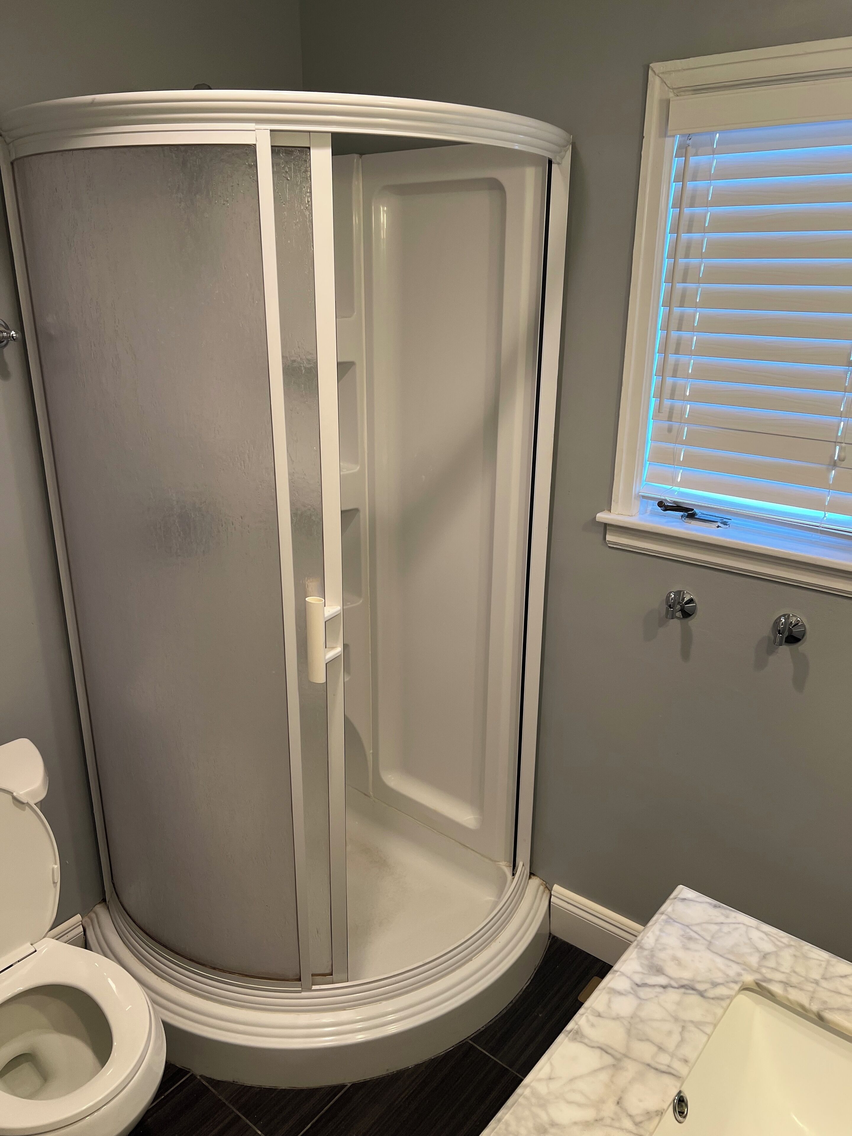 Ein Badezimmer mit Duschkabine, Toilette und einem Fenster mit Jalousien.